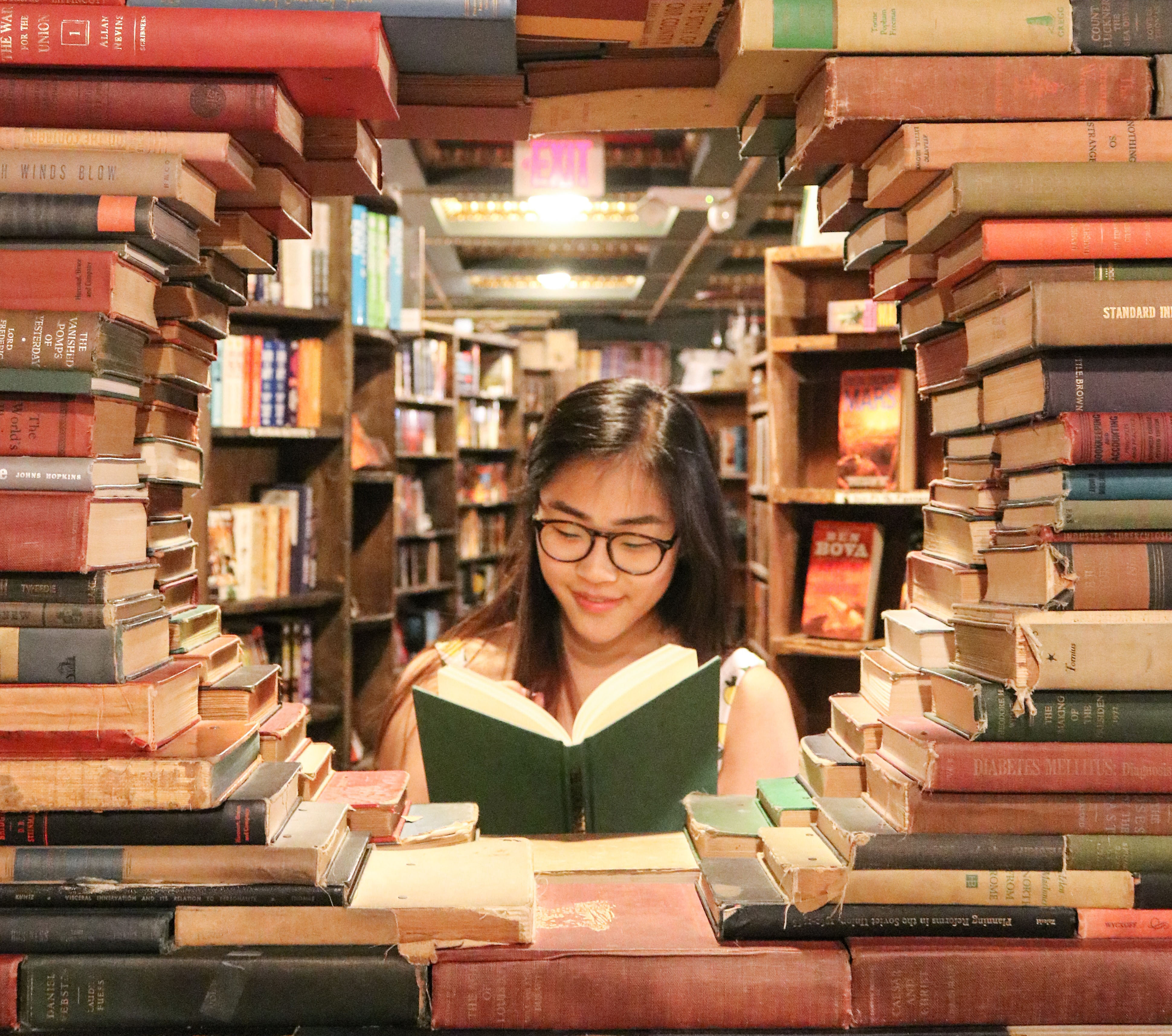 Young woman reading a book by stacks of books