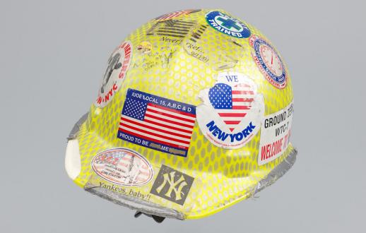 The hat is composed of a white plastic covered in a peeling yellow and silver reflective material. The exterior of the hat is covered in stickers and signatures.