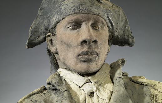 Standing male figure in military unitform wearing a blue hat with cockade