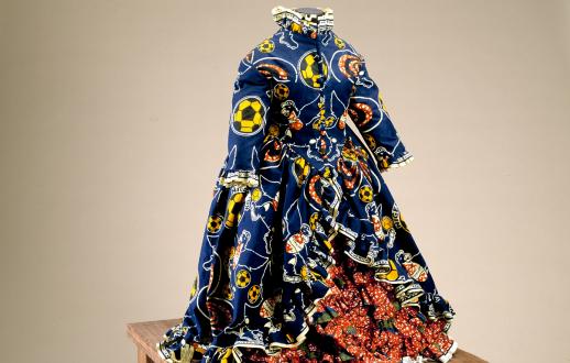 Mannequin of a young girl without a head and dressed in a Victorian style dress made from brightly colored contemporary printed fabric decorated with a soccer ball and flower pattern.