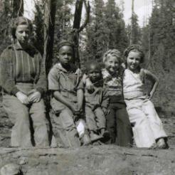 Black and white image of children sitting on a log.