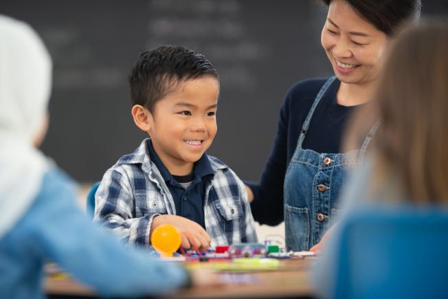 A young boy looking at his teacher from his desk in a classroom