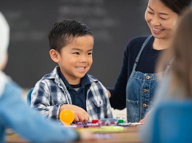 A young boy looking at his teacher from his desk in a classroom