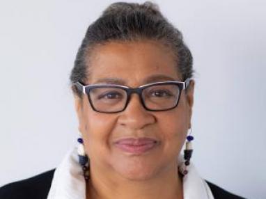 Black woman wearing glasses, a black jacket and a white blouse.